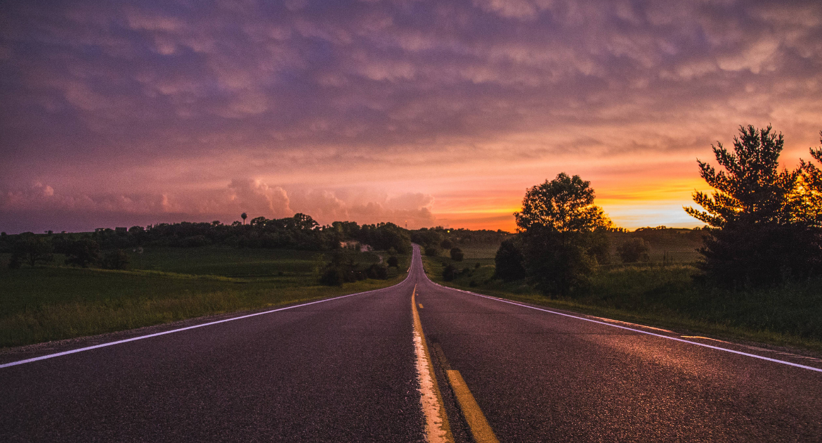 A photo of a road at sunset. There are double yellow lines in the middle of the road.